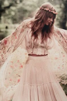 a woman wearing a white dress and a flower crown standing in the woods with her arms outstretched