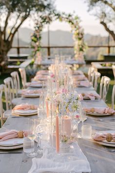 a long table is set with candles, plates and napkins for an outdoor dinner