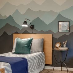 a bedroom with mountains painted on the wall and a small night stand next to it