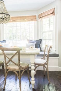 a dining room table with two chairs and a bench in front of the window,