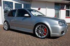 a silver car parked in front of a white building with red rims on it