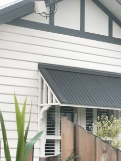 a white house with a black roof and shutters on the front door is next to a green plant