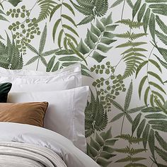 a bed with white sheets and pillows in front of a green leafy wallpaper