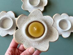 a hand holding an egg in a flower shaped bowl next to other small ones on a table