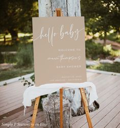 an easel with a sign that says welcome to the baby on it, sitting in front of a tree