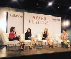 four women sitting on couches in front of a power players banner at an event