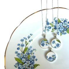 three necklaces are hanging on a plate with blue flowers and leaves painted on it