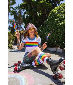 a woman sitting on the ground with her skateboard and holding two rainbow colored lollipops