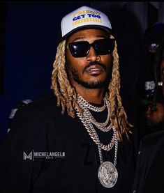 a man with dreadlocks wearing a hat and sunglasses standing next to another man