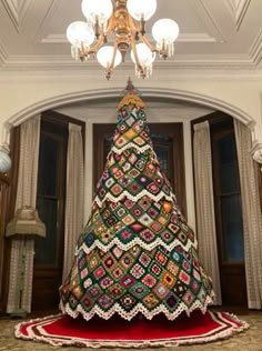 a christmas tree made out of crochet is displayed in a room with chandelier