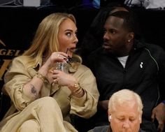 a man and woman sitting next to each other at a basketball game, one holding a drink in her hand