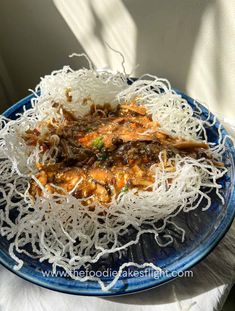 a blue plate topped with noodles and meat on top of a white cloth covered table