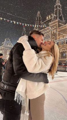 a man and woman kissing in front of an ice rink with lights strung above them