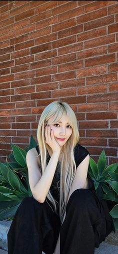 a woman sitting on the ground in front of a brick wall with her hand under her face