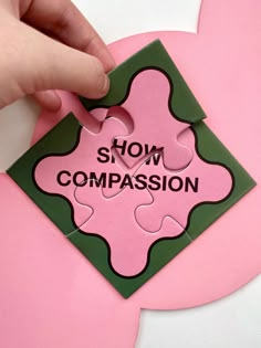 a piece of pink paper with the words show compassion on it being held by someone's hand