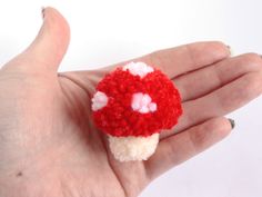 a hand holding a tiny red and white mushroom