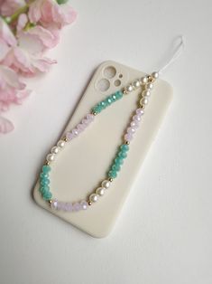 a cell phone with some beads on it next to pink flowers and a white case