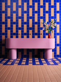 a pink bench sitting in front of a blue tiled wall