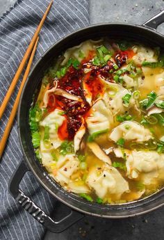 a pot filled with dumplings and vegetables next to chopsticks