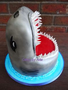 a shark cake on a blue plate next to a brick wall