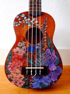 an ukulele with flowers painted on it sitting on top of a wooden floor