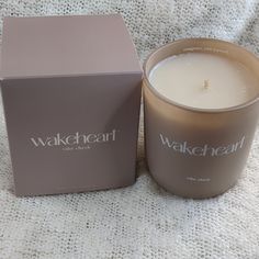 a candle sitting next to a box on a white cloth covered bed sheet with the words wakeheal written on it