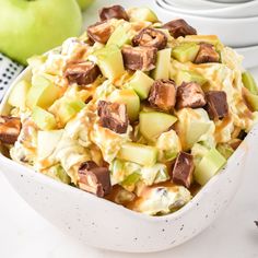 a white bowl filled with apple salad next to two green apples