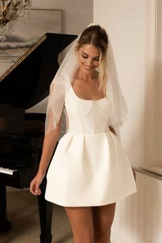 a woman in a short white dress standing next to a piano