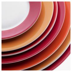 a stack of orange and pink plates sitting next to each other on a white surface