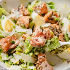 a salad with salmon and lettuce in a white bowl on top of a table