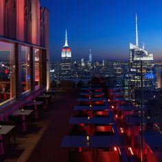 the city skyline is lit up at night with red lights on tables and benches in front of them