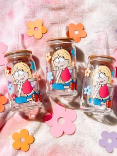 three glass jars with cartoon characters on them sitting on a pink and white blanket surrounded by flowers