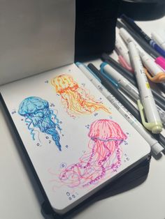 an open notebook with colored pencils next to it and some markers on the desk