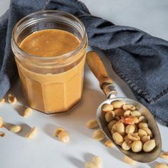 a jar of peanut butter next to a spoon with peanuts