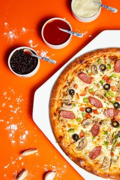 a pizza sitting on top of a white plate covered in toppings next to condiments