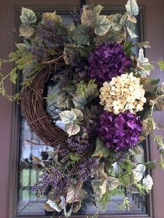 a wreath with purple flowers and greenery hanging on a front door window sill