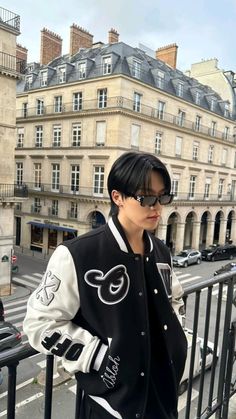 a man with black hair and glasses is standing on a balcony in front of some buildings