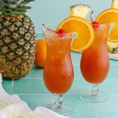 two glasses filled with orange juice and garnished with a pineapple on the side