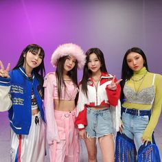 four young women posing for a photo in front of a purple background with one pointing at the camera