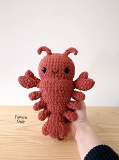 a hand holding a red crocheted stuffed animal on top of a wooden table