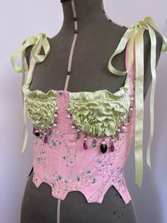 Made-to-order & historically inspired scalloped bustier. Corseted bodice in japanese sakura blossom print cotton, boned with a mixture of polyester and steel boning.  Pastel green silk satin cups, ruched with elastic for a stretchy and snug fit.  Embellished by hand around the cups with a mixture of freshwater pearls and glass crystal beading. Includes 2 gorgeous lanpwork beads, 1 blackberry and 1 blueberry. Lace up back and tie straps fastened with satin ribbon. I would recommend sending me you Corset Bustier Top, Green Corset, Velvet Corset, Pink Cherry Blossom, Pink Corset, London Spring, Corset Bustier, Corset Lingerie, Pink Blossom