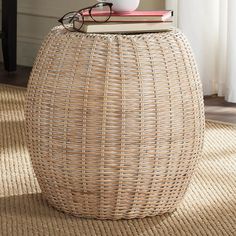 a wicker stool with eyeglasses on top and books sitting on it in front of a window