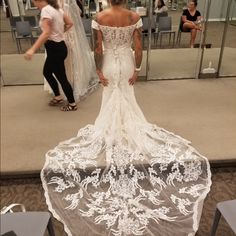 a woman standing in front of a mirror wearing a wedding dress with an off the shoulder design