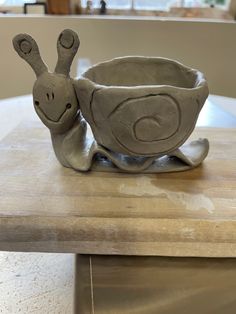 a clay sculpture of a snail sitting on top of a wooden table next to a bowl