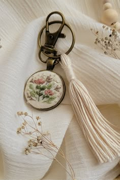 a tasseled keychain with flowers on it sitting on top of a white cloth