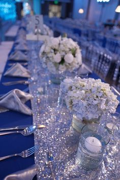 the table is set with silverware and white flowers in glass vases on it