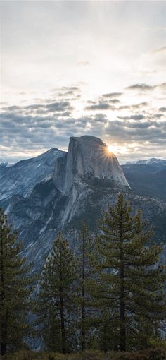 the sun shines brightly through the clouds over a mountain range with pine trees and mountains in the background