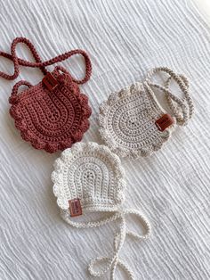 three crocheted purses sitting on top of a white bed next to each other