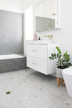 a bathroom with white and gray tile walls, flooring and a plant next to the toilet