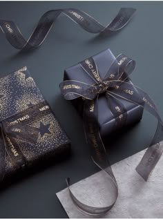 two wrapped presents are sitting on a table next to a silver envelope with a ribbon